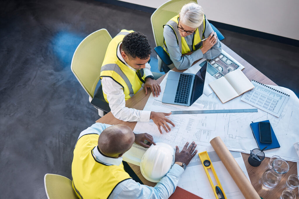 Construction team reviewing blueprints and laptop at a conference table representing cybersecurity protocol review for construction firms